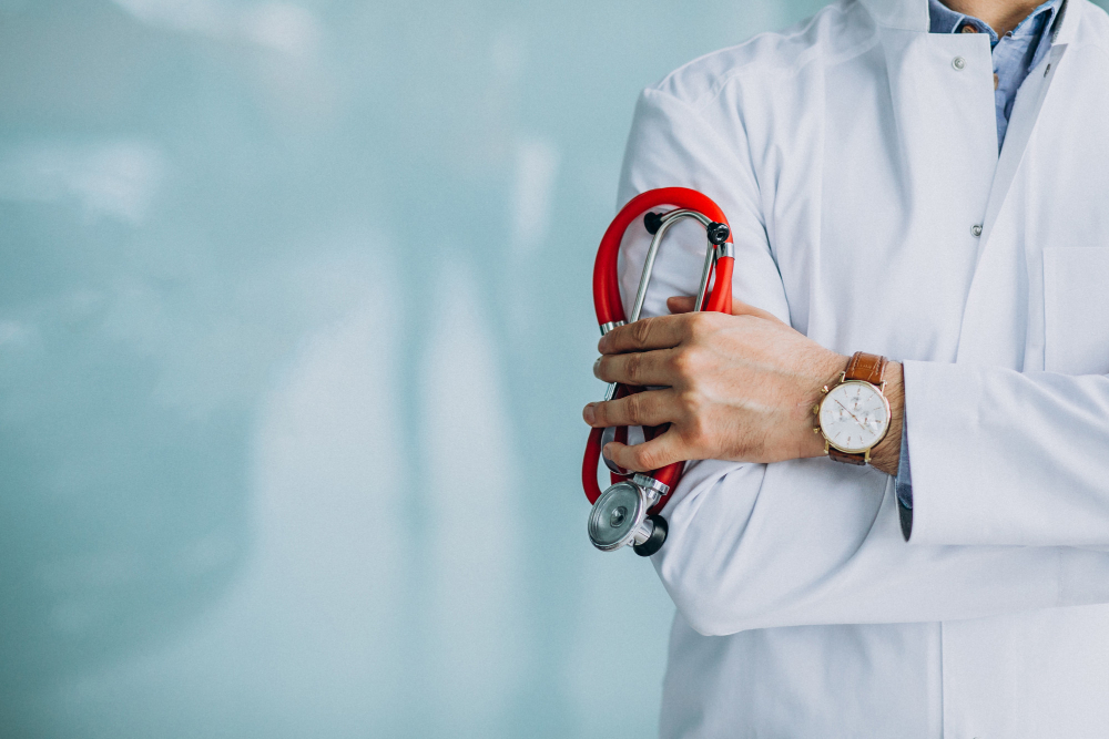 Doctor in a white coat holding a red stethoscope with arms crossed.
