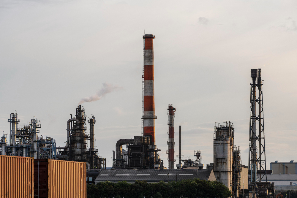 Industrial refinery complex with tall chimneys and metal structures under a cloudy sky.