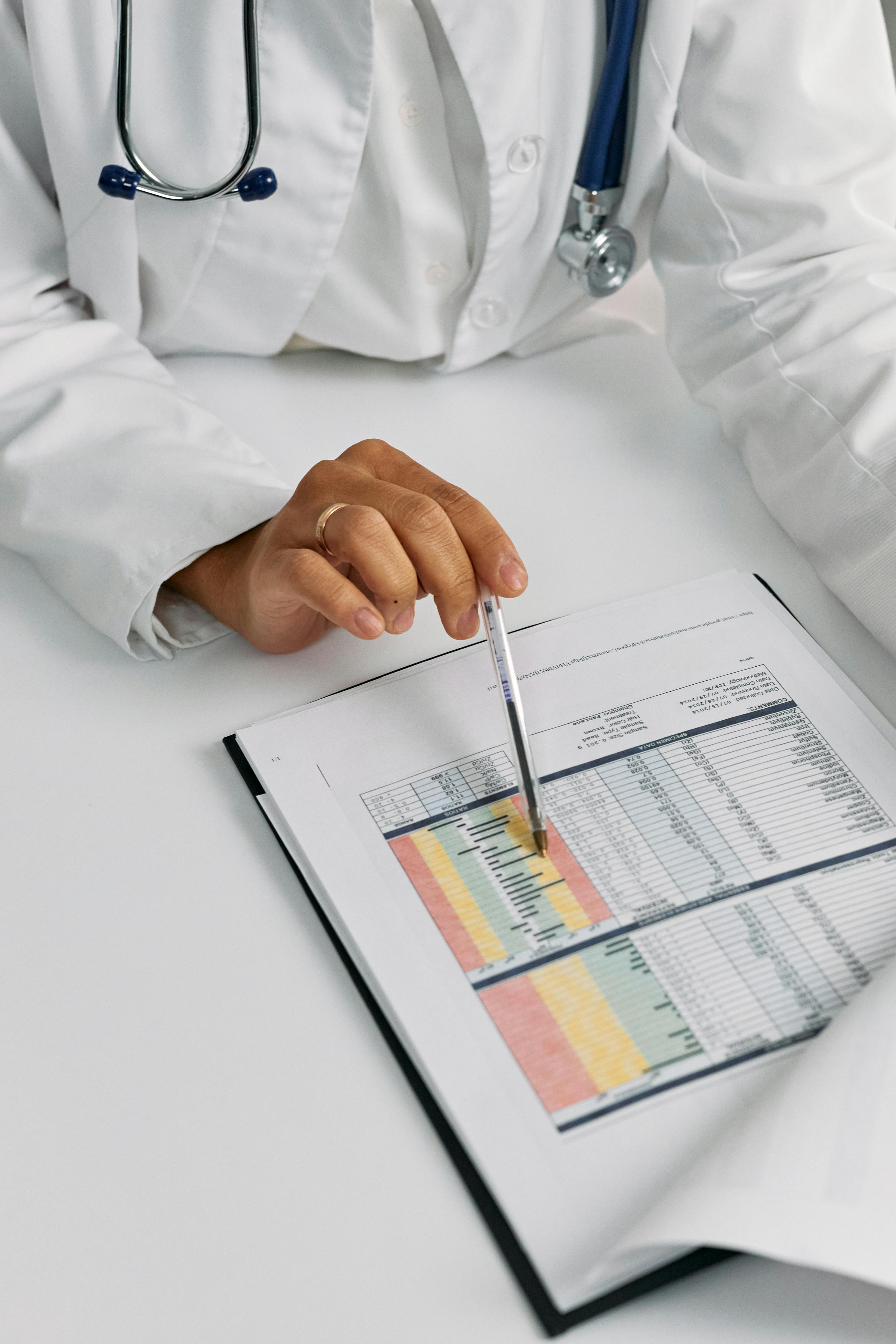 Doctor in white coat pointing at medical data charts in a report with a pen.